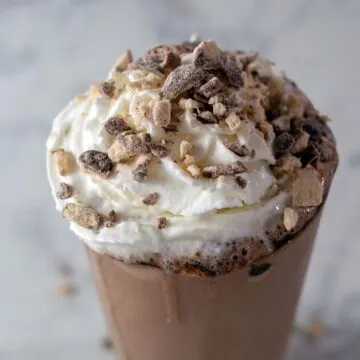 A triple chocolate malt milkshake garnished with whipped cream and crushed malted milk candies