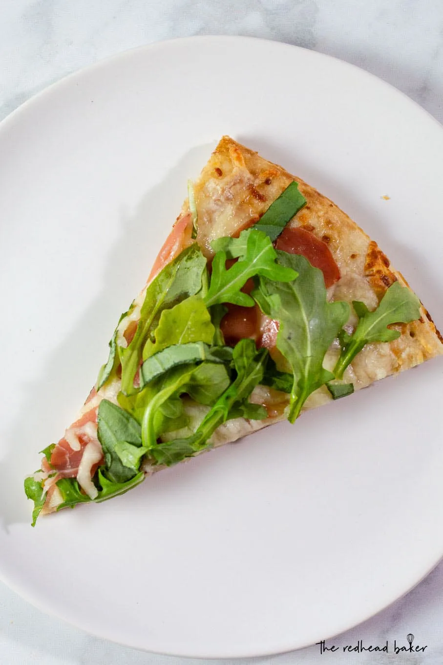 An overhead photo of a slice of white pizza with prosciutto and arugula