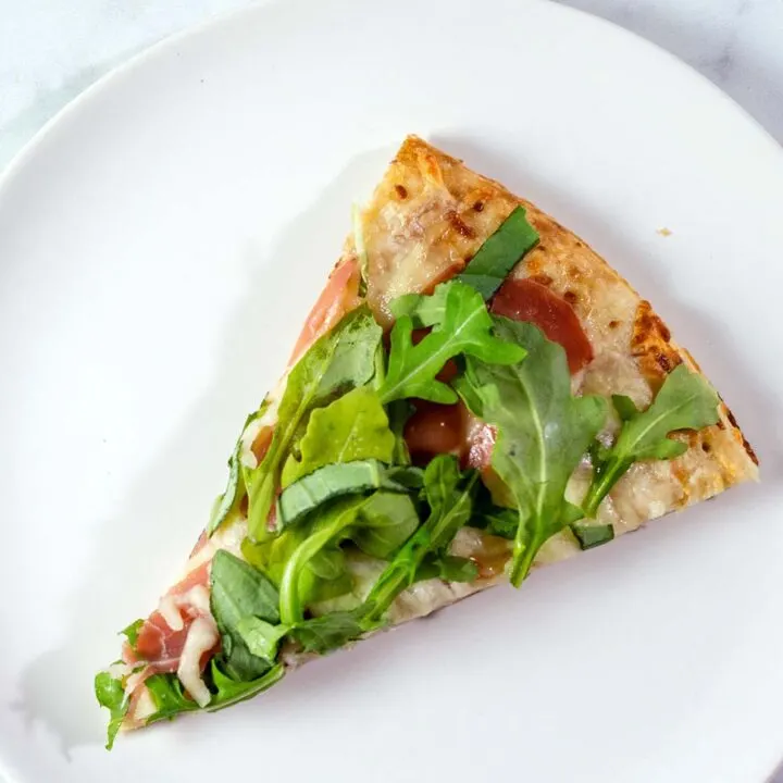 An overhead photo of a slice of white pizza with prosciutto and arugula