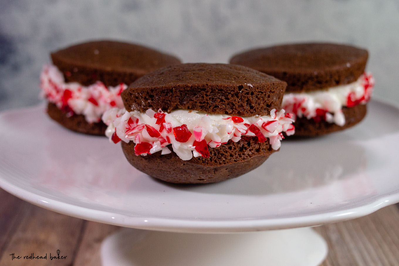 Three chocolate peppermint whoopie pies on a white cake plate
