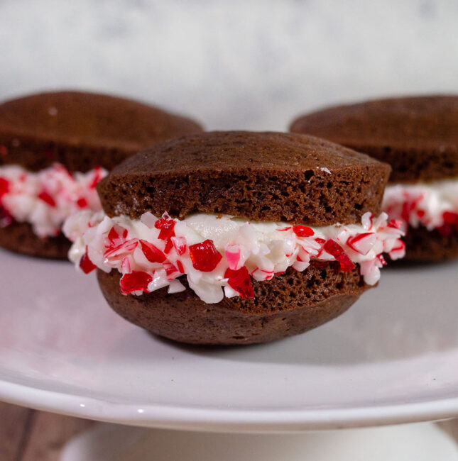 Three chocolate peppermint whoopie pies on a white cake plate