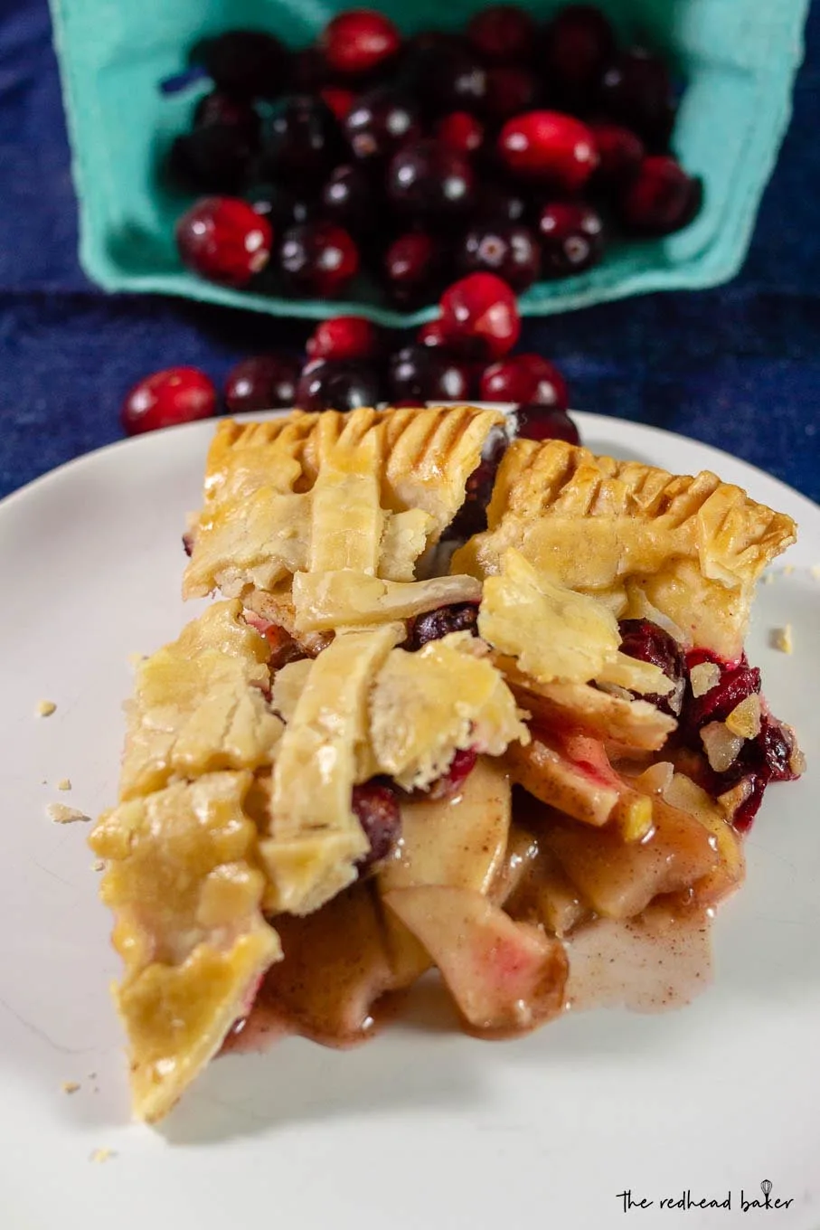 A slice of cranberry apple pie in front of a container of cranberries