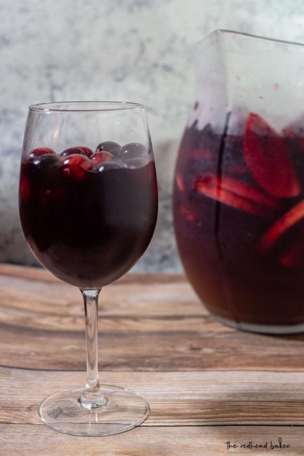 A glass of cranberry apple sangria in front of a pitcher