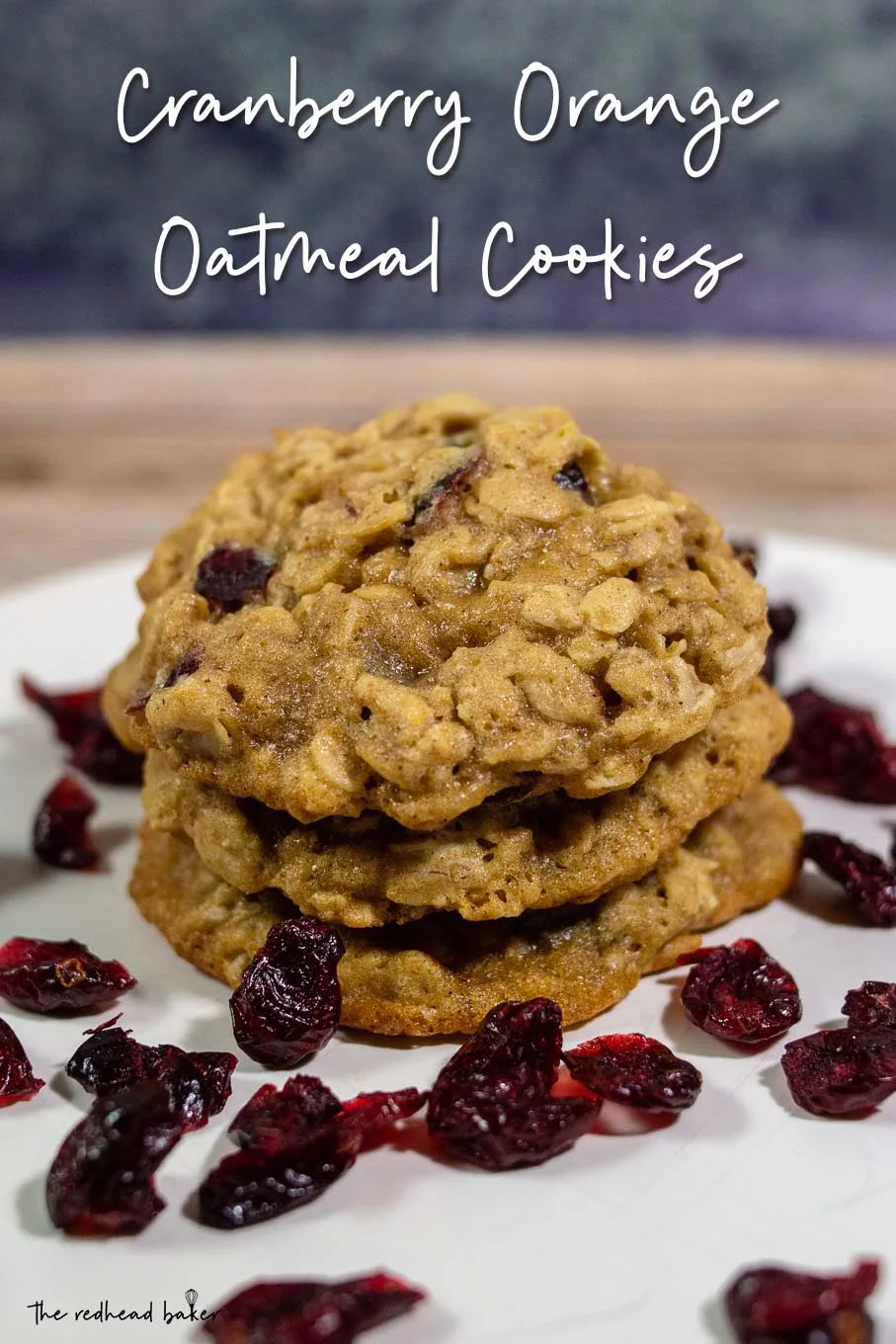 Three cranberry-orange oatmeal cookies in a stack surrounded by dried cranberries