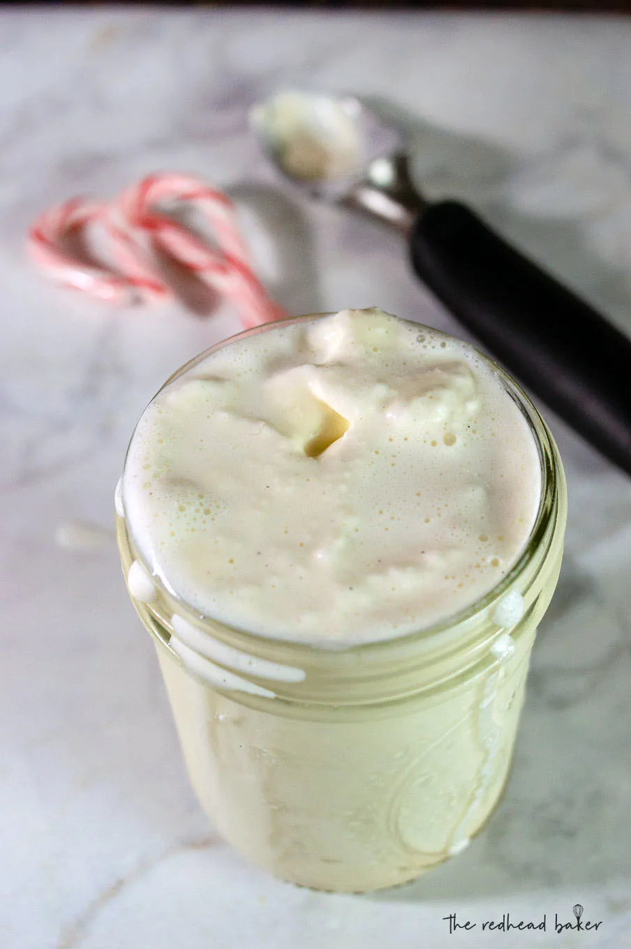 A candy cane crunch milkshake with an ice cream scoop and two candy canes in the background