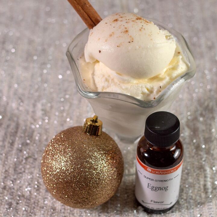 A dish of eggnog gelato, a bottle of Lorann Eggnog Flavor, and a glittery gold Christmas ornament