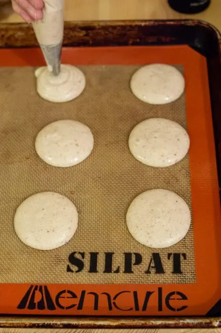 Piping shells for eggnog macarons onto a Silpat silicone baking mat