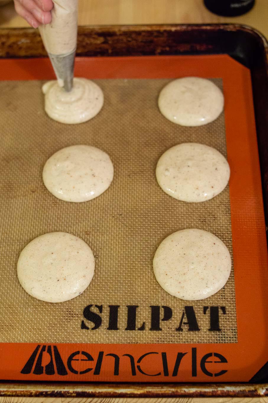 Piping shells for eggnog macarons onto a Silpat silicone baking mat