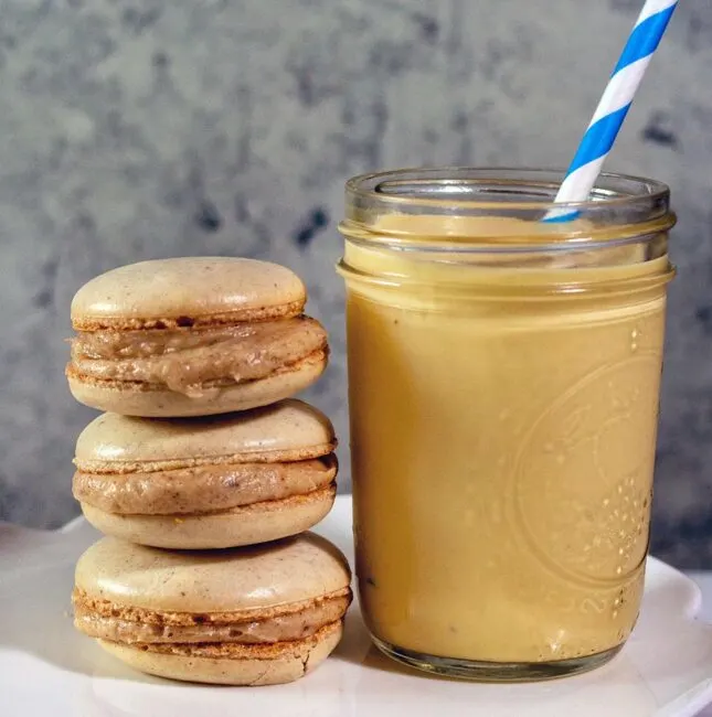 Three eggnog macarons stacked next to a mason jar of eggnog