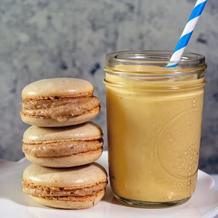 Three eggnog macarons stacked next to a mason jar of eggnog