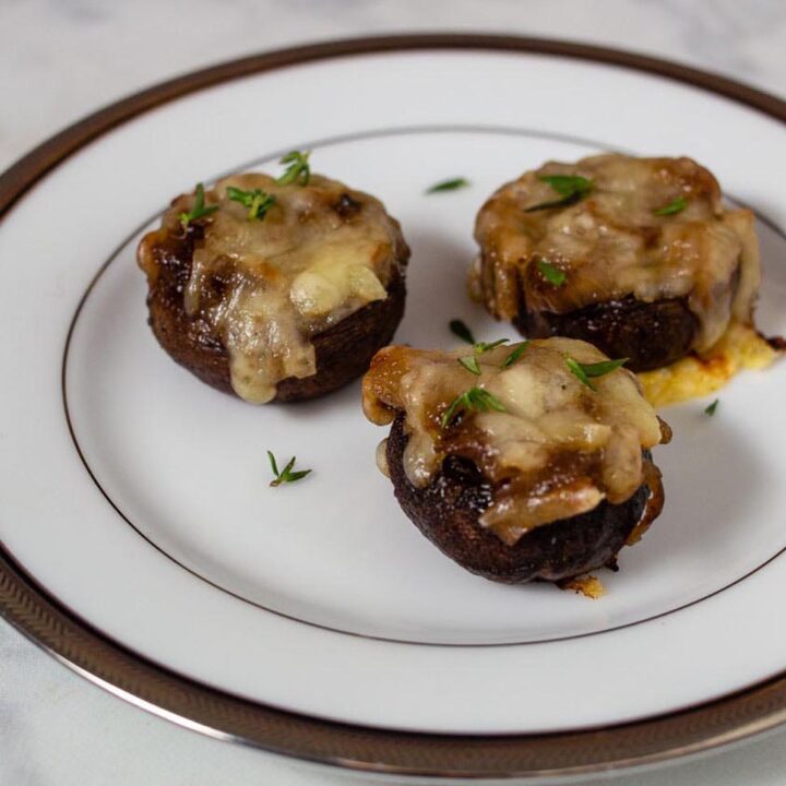 Three French onion stuffed mushrooms on a small white plate