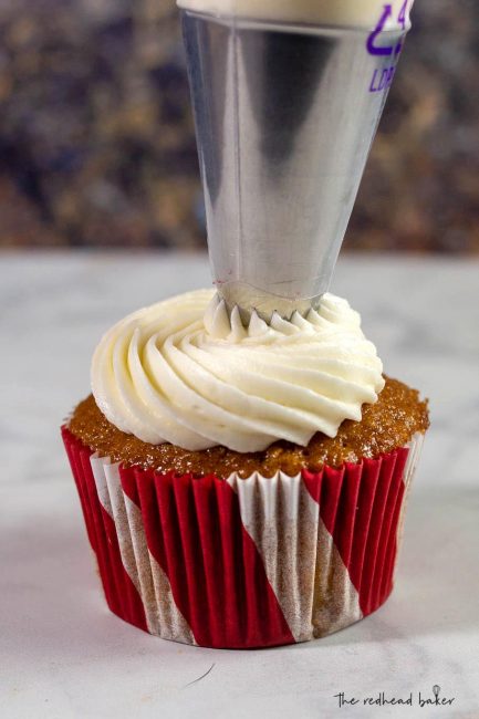 Sweetened cream cheese frosting being piped onto a gingerbread cupcake