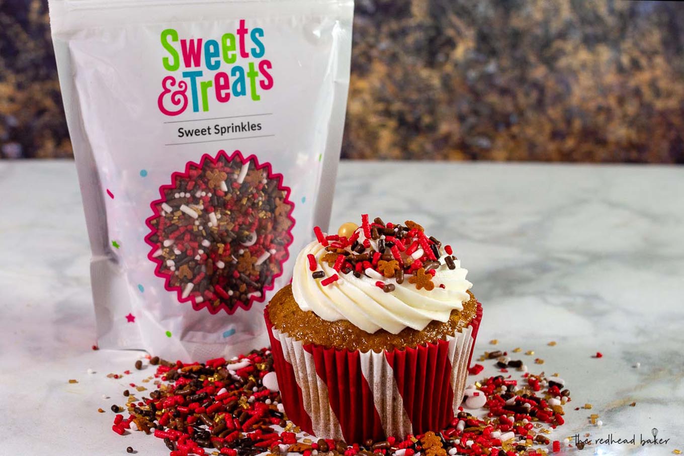 A gingerbread cupcake with cream cheese frosting in front of a bag of Sweets and Treats gingerbread sprinkles