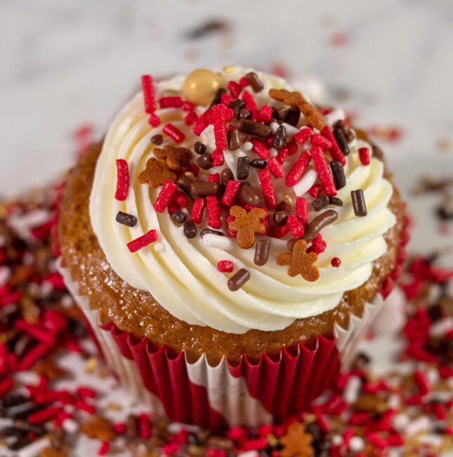 A gingerbread cupcake with cream cheese frosting, in a pile of Sweets and Treats gingerbread sprinkles
