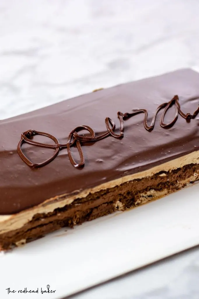 A whole chocolate opera cake on a white serving tray