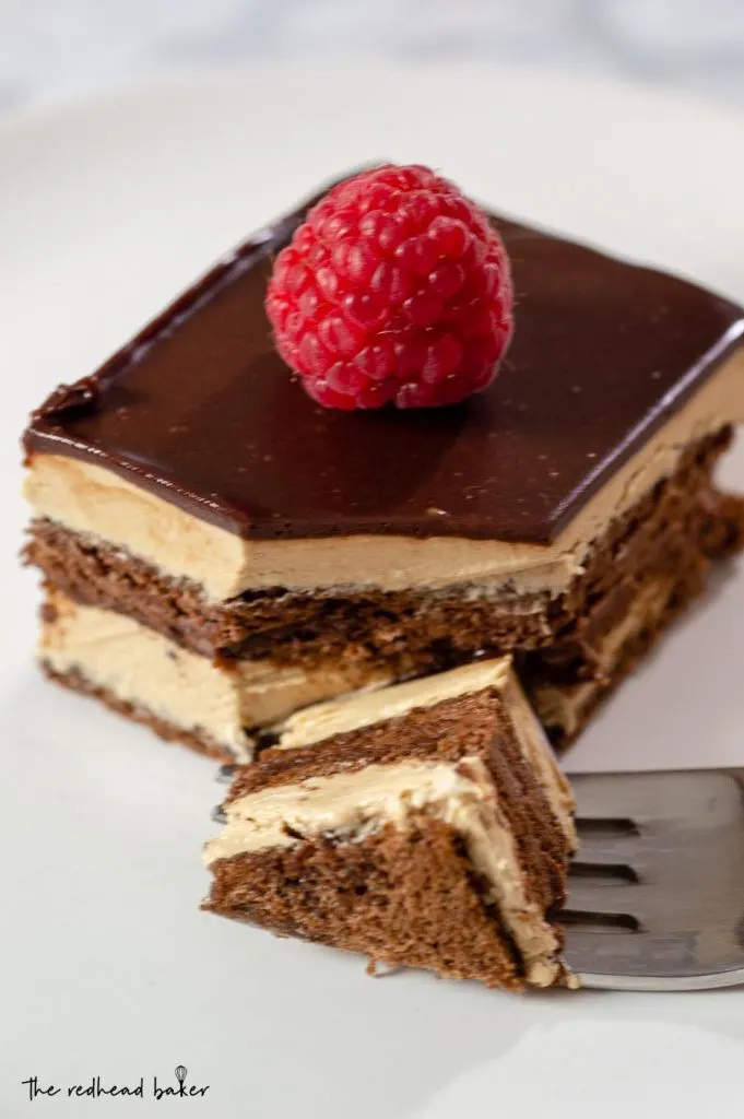 A slice of chocolate opera cake with a corner of the slice on a fork