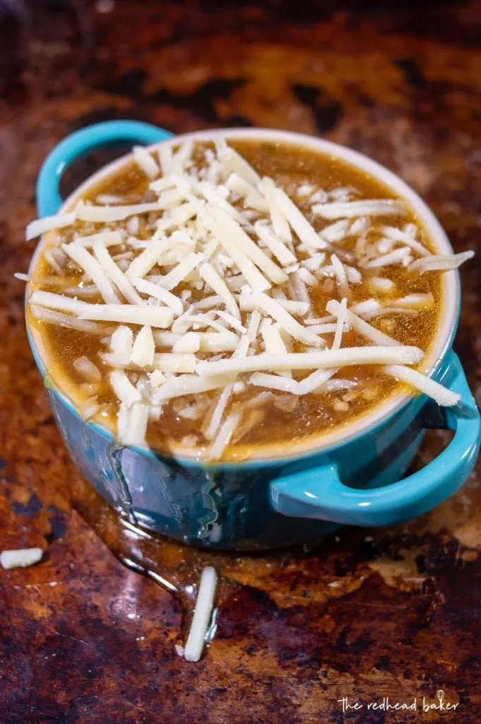 A cocette of French onion soup on a baking sheet with shredded Gruyere cheese on top