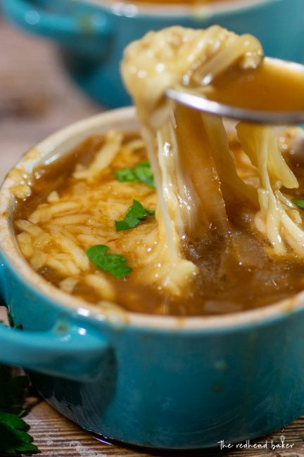 A photo of a spoon lifting the melty cheese up from the cocette of French onion soup
