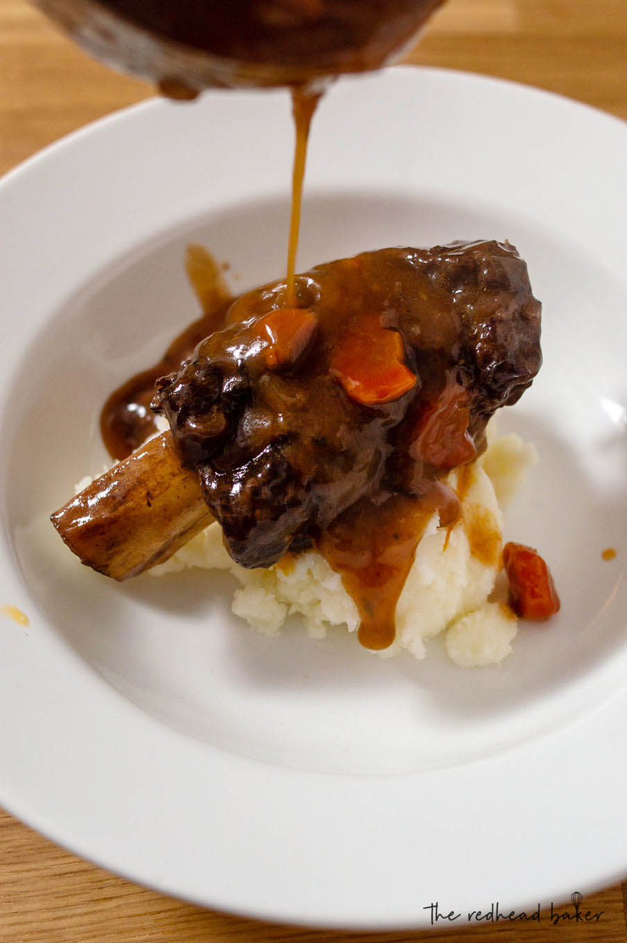 A short rib on the bone over mashed potatoes with gravy being poured over top.