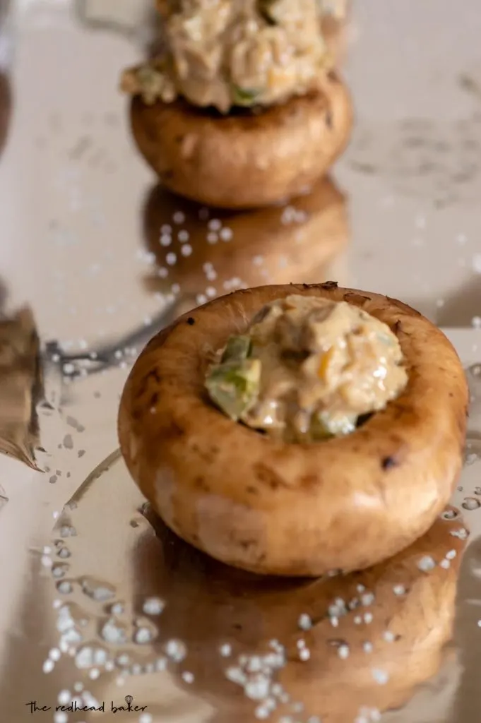 Mushroom caps on a baking sheet being stuffed with jalapeno popper mixture