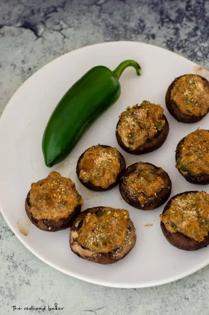 An overhead shot of a plate of jalapeno popper stuffed mushrooms and a whole jalapeno pepper