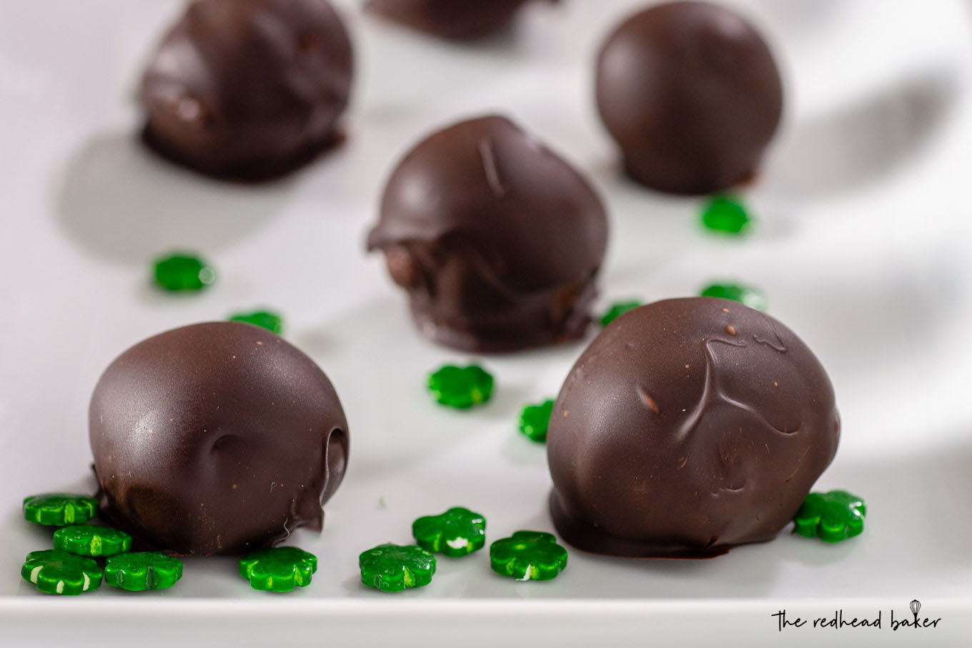 Several Irish cream truffles on a white plate surrounded by shamrock sprinkles.