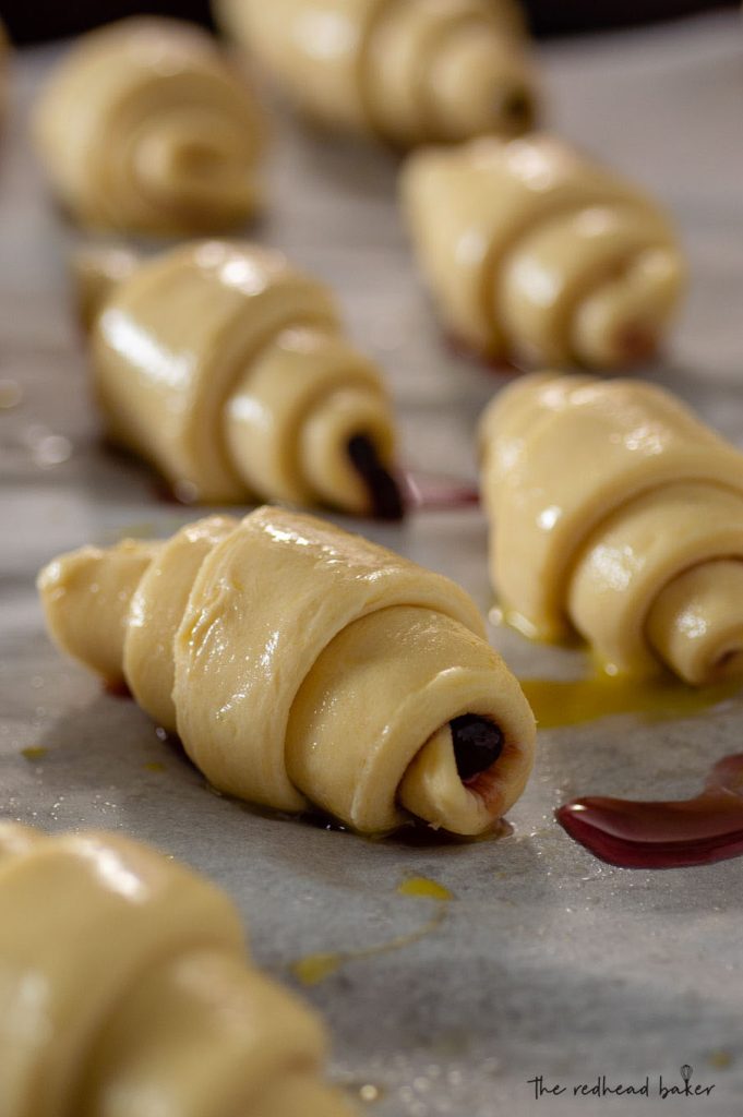 Shaped raspberry brioche crescents, egg-washed and proofing on a baking sheet