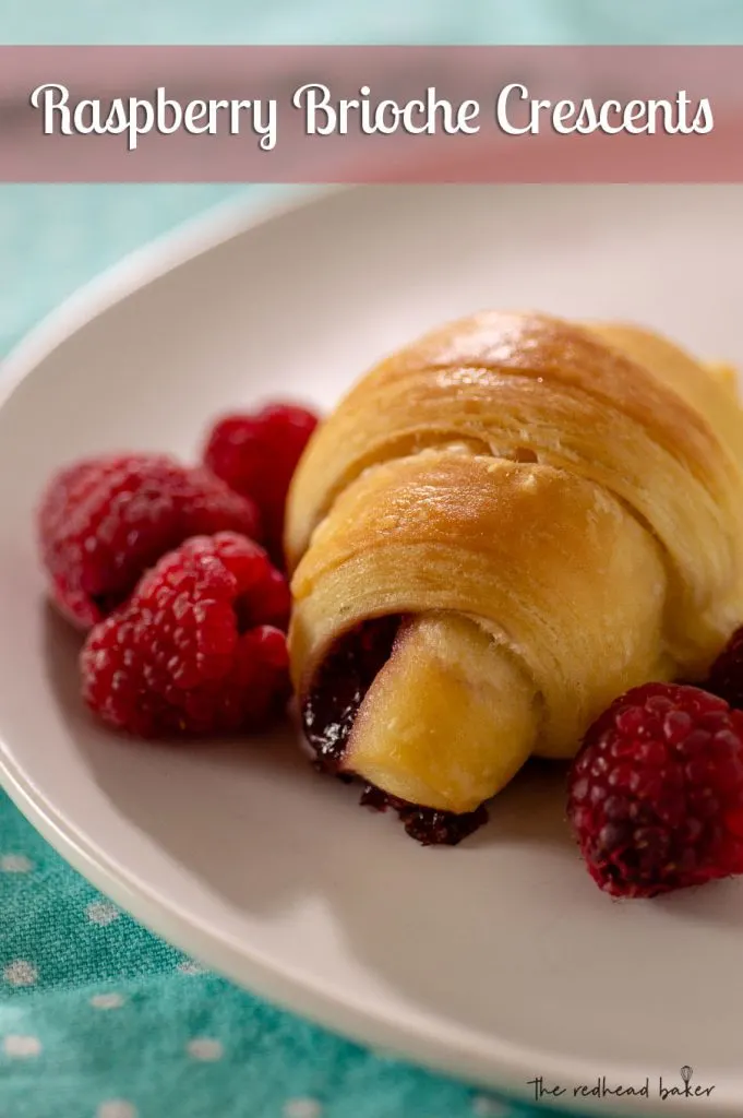 A raspberry brioche crescent on a plate with fresh raspberries