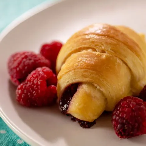 Raspberry brioche crescent on a plate with fresh raspberries