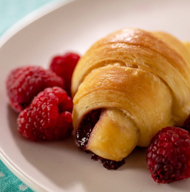 Raspberry brioche crescent on a plate with fresh raspberries