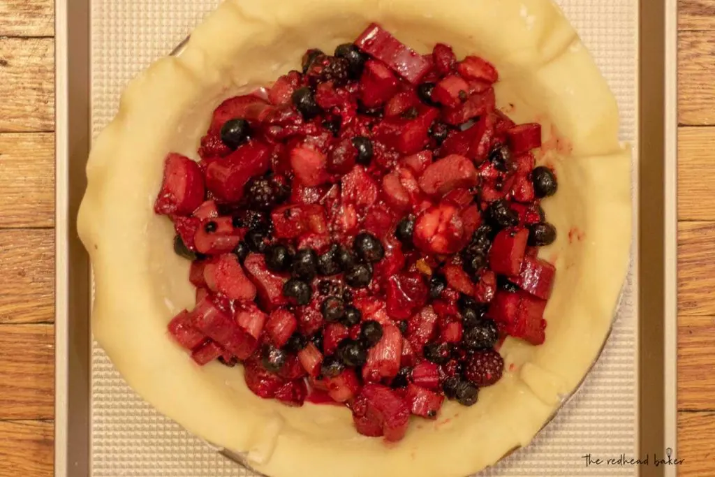 An unbaked rhubarb berry pie without its top crust on a baking sheet