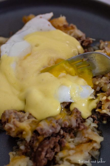 A fork cutting into the fried egg on top of the breakfast poutine