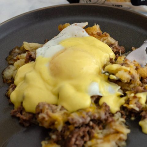 A plate of breakfast poutine topped with a fried egg and Hollandaise