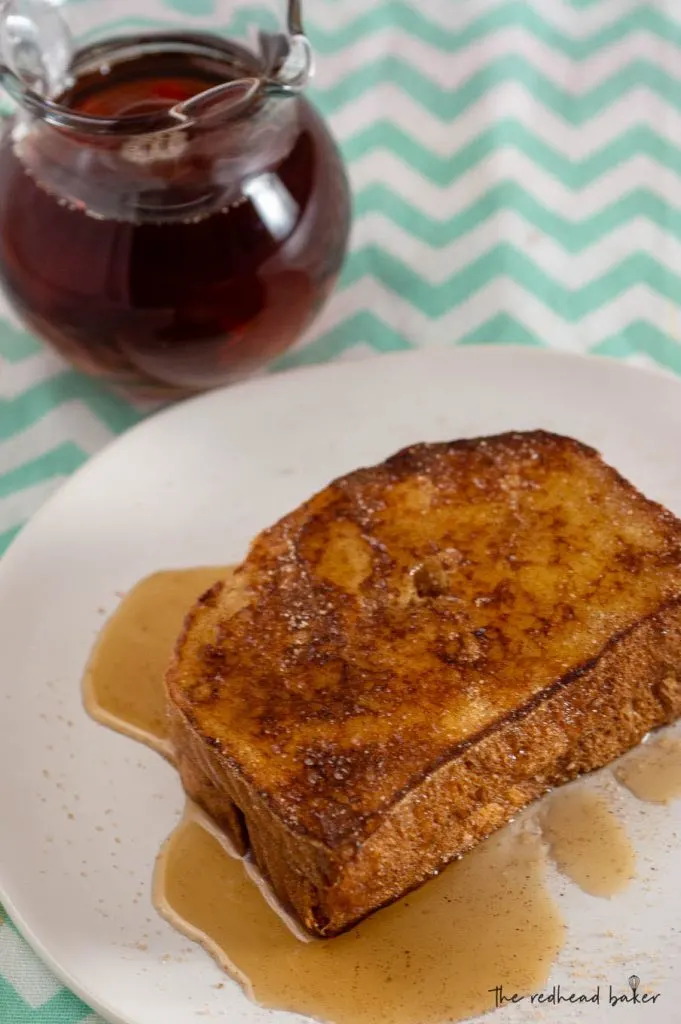 An overhead view of two slices of churro French toast on a white plate in front of a pitcher of syrup