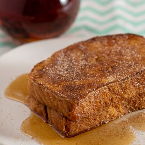 Two slices of churro French toast in front of a pitcher of syrup
