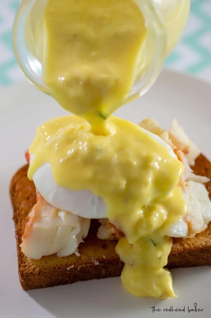 Crab hollandaise being poured over lobster eggs benedict