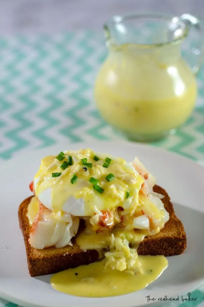 A plate of lobster eggs benedict in front of a pitcher of crab hollandaise sauce