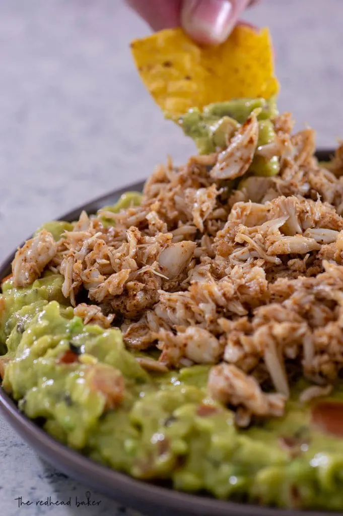 A hand dips a tortilla chip into the spicy crab guacamole