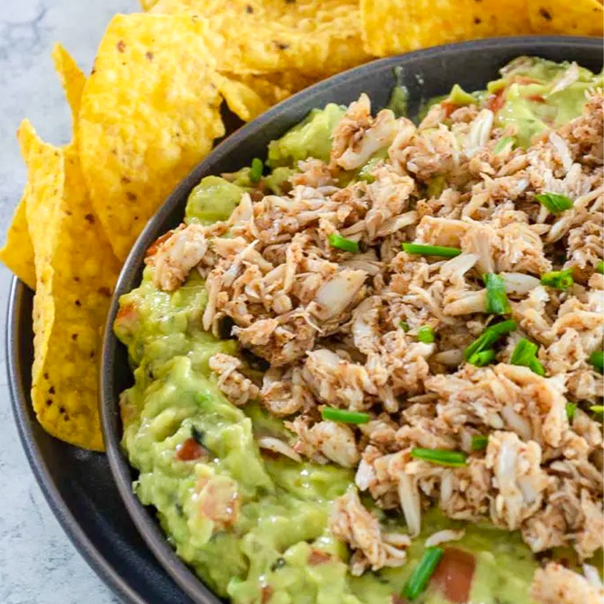 A dish of spicy crab guacamole surrounded by tortilla chips.