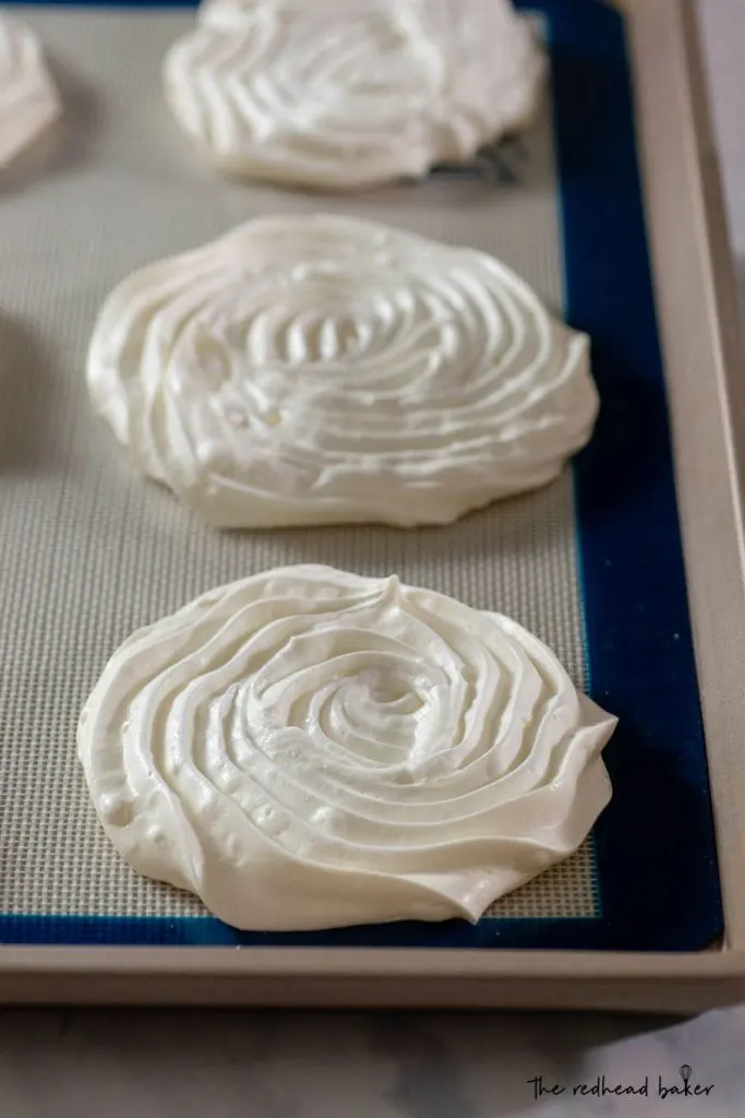 Three plain white pavlova meringue bases on a baking sheet
