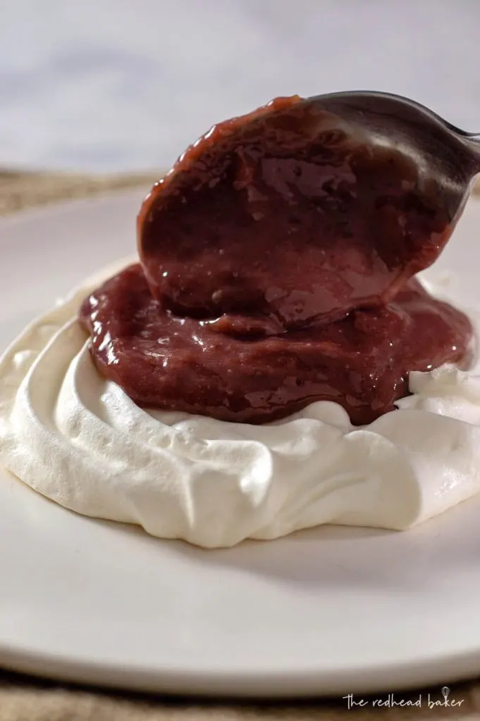 Cherry-lime curd being spooned onto a meringue pavlova base