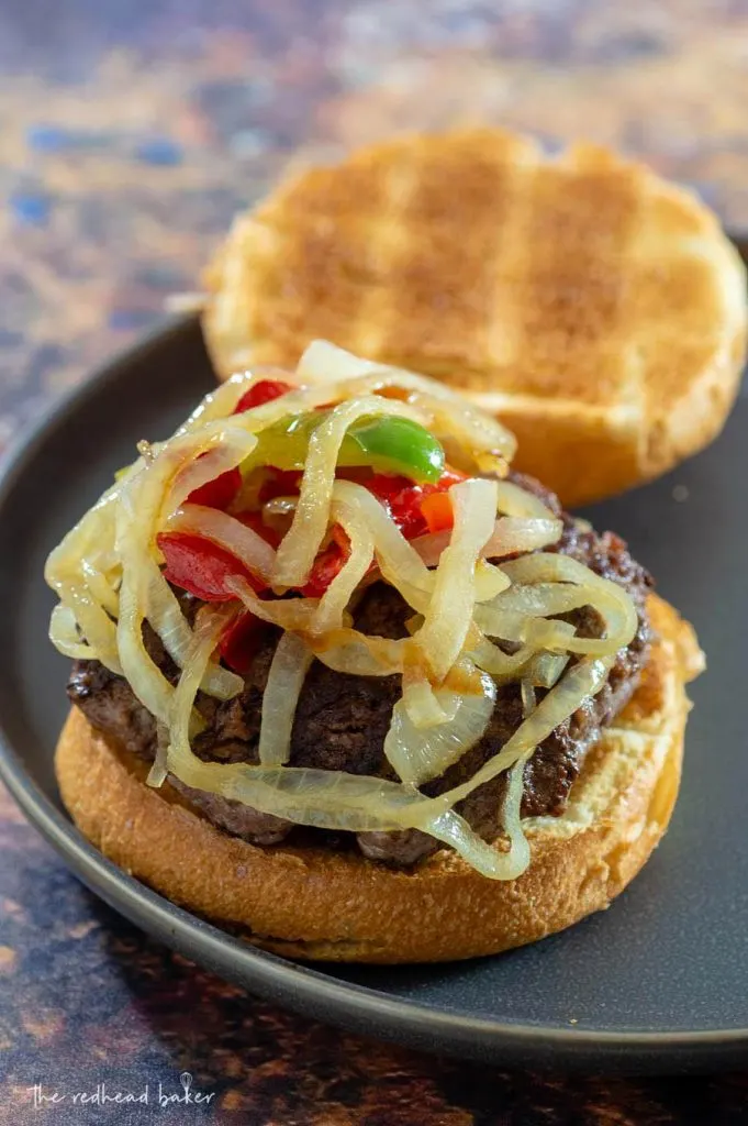 An open Philly burger, with a beef patty and fried onions and peppers, waiting for cheese sauce