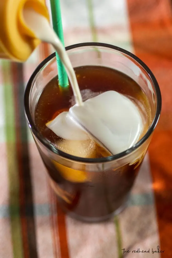 An overhead shot of coffee creamer pouring into a glass of caramel cold brew.