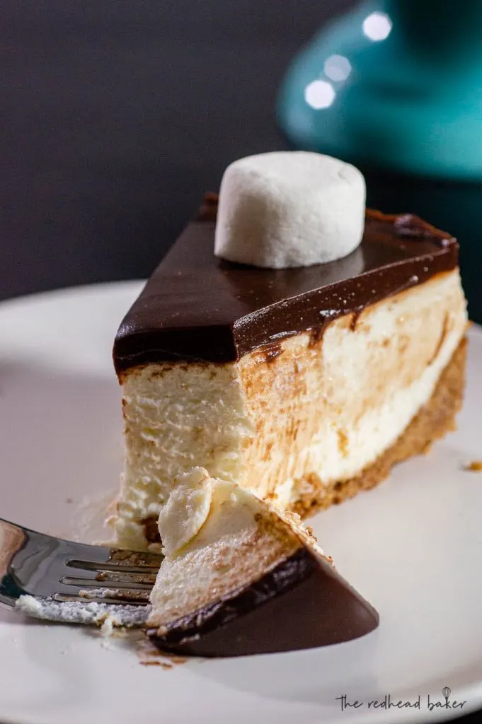 A slice of smores cheesecake on a plate with a fork