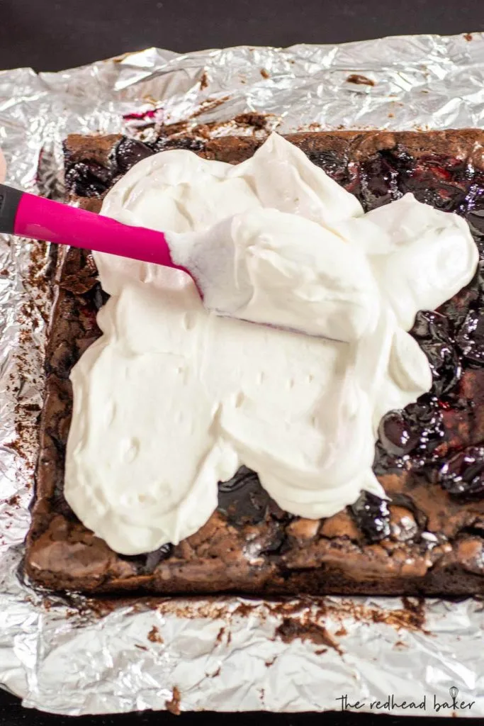 Whipped cream being spread onto black forest brownies