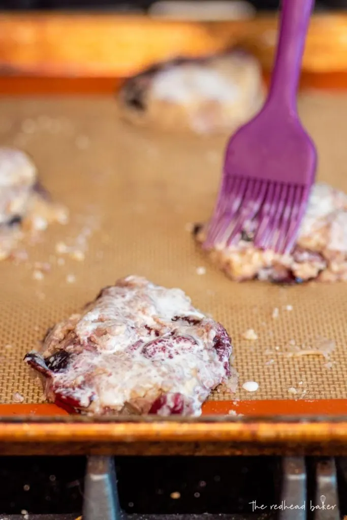 Scones on a baking sheet being brushed with cream