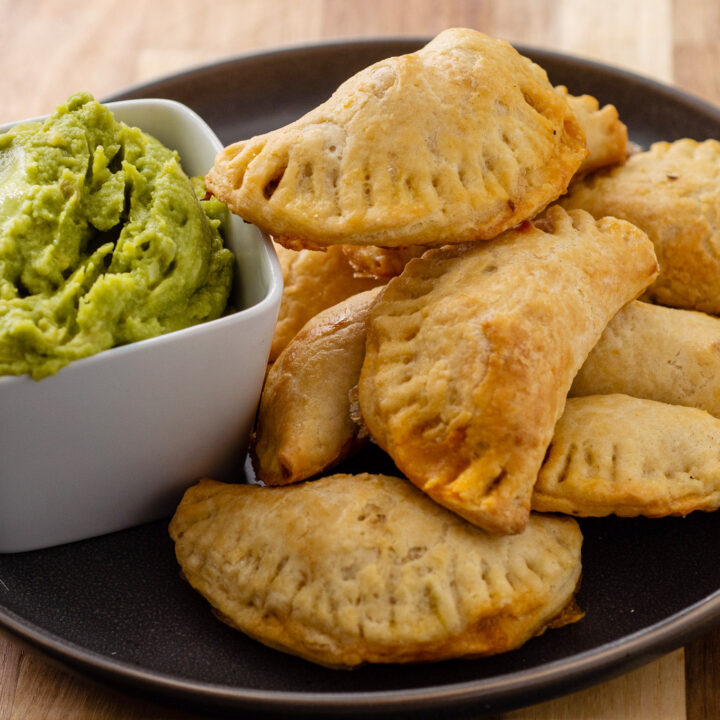 A plate of empanadas next to a bowl of guacamole.