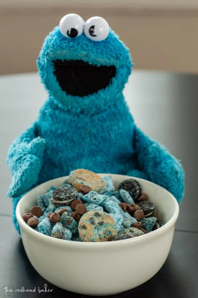 A bowl of Cookie Monster muddy buddies in front of a Cookie Monster plush toy