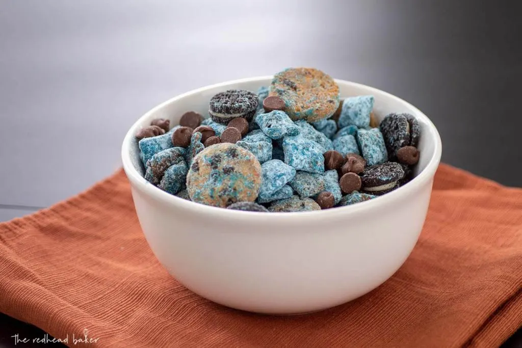 A bowl of Cookie Monster Muddy Buddies on an orange napkin