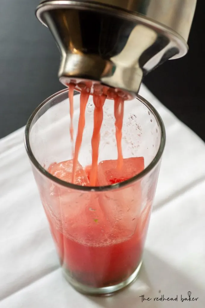 Watermelon coconut mojito pouring out of a cocktail shaker into a tall glass